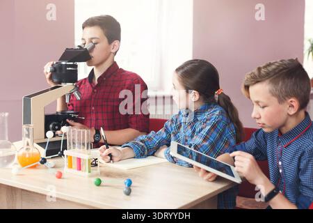 Schüler führen ein Experiment mit Mikroskopen und Tablets im Klassenzimmer durch Stockfoto