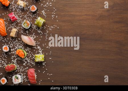 Sammlung von Sushi-Stücken auf hölzerner Oberfläche mit verstreuten Sesam-Samen Stockfoto