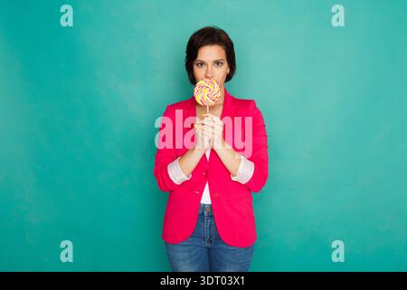 Die junge Frau hält Lutscher vor ihrem Gesicht vor einem hellen Hintergrund Stockfoto