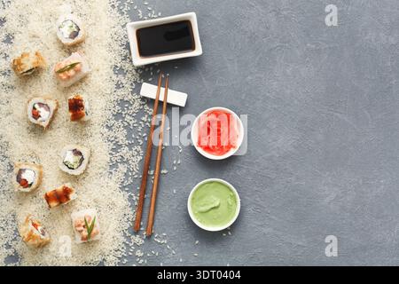 Sushi-Brötchen auf grauer Oberfläche mit Sojasauce, Wasabi und Ingwer auf Seiten mit Reis Stockfoto