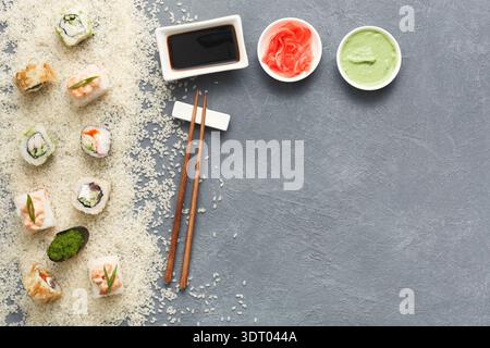 Sushi-Brötchen mit Würzmitteln und Stäbchen, die während der Zubereitung der Mahlzeiten auf einer grauen Oberfläche angeordnet sind Stockfoto