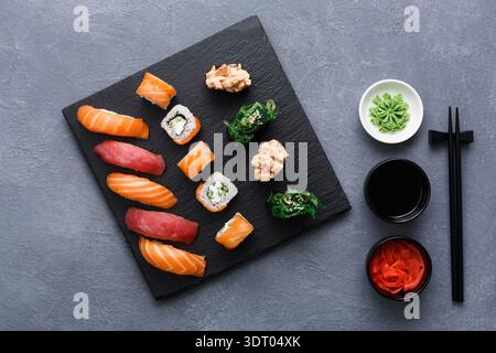 Sushi-Platte serviert mit Soßen und Würzmitteln auf einem schwarzen Steinbrett Stockfoto
