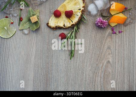 Sammlung von Früchten und Kräutern auf einer Holzfläche mit Eiswürfeln und Blumen Stockfoto