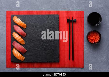 Sushi-Auswahl auf einer Steinplatte mit Stäbchen und Seiten auf einer roten Matte Stockfoto