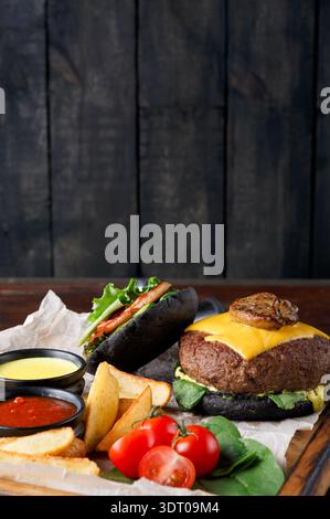 Kreative Burger-Präsentation mit schwarzem Brötchen und leckeren Beilagen auf Holztisch Stockfoto