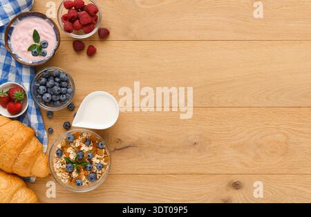 Frühstückskollektion mit Beeren, Joghurt und Croissants auf einem Holztisch Stockfoto