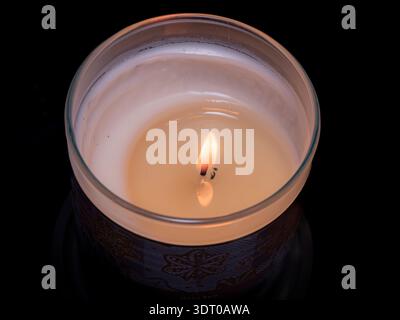 Nahaufnahme einer beleuchteten Kerze in einem Glashalter vor schwarzem Hintergrund, die Ruhe, Reflexion und Wärme symbolisiert Stockfoto