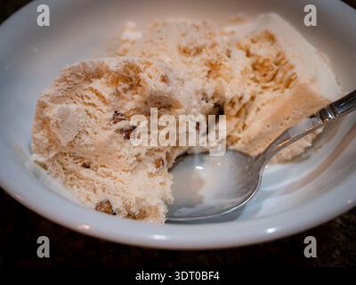 Nahaufnahme von Butterpecan-Eislöffeln in einer weißen Schüssel mit einem Löffel, die cremige Textur und Nussstücke zeigen Stockfoto
