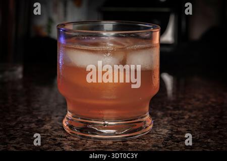Nahaufnahme eines Whiskeys oder Cocktails mit Eiswürfeln in einem klaren Glas auf einer dunklen Bartheke, die Entspannung und Lifestyle-Genuss symbolisieren Stockfoto