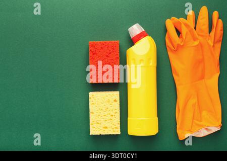 Reinigen Sie Verbrauchsmaterialien, die in einem Set auf grünem Hintergrund angeordnet sind und Schwämme, Handschuhe und Reiniger zeigen Stockfoto