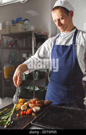 Küchenchef kocht verschiedene Gerichte in einer professionellen Küche mit einer Auswahl an Zutaten Stockfoto
