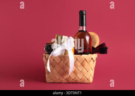 Geschenkkorb mit männlichen Accessoires, Flasche Wein und Geschenk auf rotem Hintergrund Stockfoto