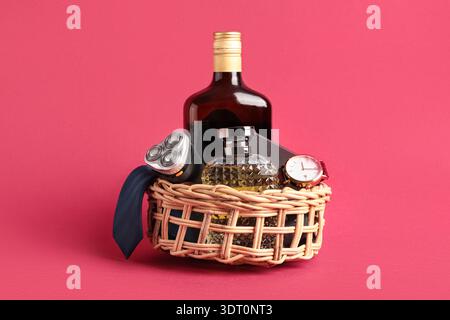 Geschenkkorb mit männlichen Accessoires, Flasche Alkohol und Parfüm auf rotem Hintergrund Stockfoto