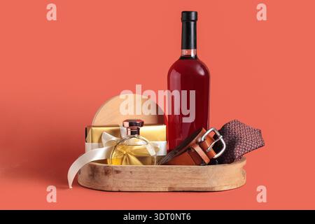 Geschenkkorb mit männlichen Accessoires, Flasche Wein und Geschenk auf rotem Hintergrund Stockfoto