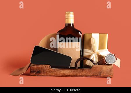 Geschenkkorb mit männlichen Accessoires, Flasche Alkohol, Geschenk und Handy auf rotem Hintergrund Stockfoto