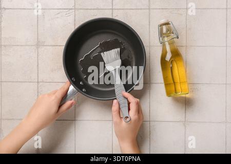 Junge Frau, die Silikonbürste und Pfanne auf weißem Fliesenhintergrund hält Stockfoto