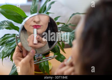 Beim Auftragen des Lippenstifts mit Reflexion in einem runden Spiegel trägt Eine Frau Lippenstift auf, während sie ihre Reflexion in einem runden Spiegel beobachtet, der von einem runden Spiegel umgeben ist Stockfoto