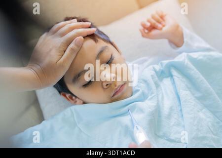 Krank, Kind und Hand mit Fieber im Schlafzimmer für Grippeinfektion, Krankheit und Schlaf mit Decken. Müde, Kind und Mutter, zu Hause für Temperatureinhaltung Stockfoto
