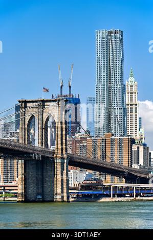 Die Brooklyn Bridge verbindet Manhattan und Brooklyn, während an klaren Tagen Skyline-Gebäude hoch im Hintergrund stehen. Stockfoto