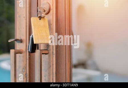 Eine Nahaufnahme eines Schlüssels für das Hotelzimmer, der in einem Schloss an einer großen Glastür hängt und den Pool reflektiert. Kopierbereich. Stockfoto