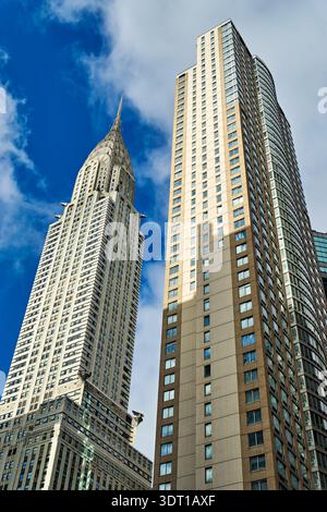 Das Chrysler Building erhebt sich in Manhattan. Nahe gelegene Gebäude reflektieren Sonnenlicht. Wolken ziehen am blauen Himmel über New York City vorbei. Stockfoto