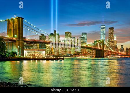 Tribute in Light zeigt bei Nacht zwei Lichtstrahlen über der Skyline von Manhattan. Die Brooklyn Bridge und die Gebäude sind in der Szene zu sehen. Stockfoto