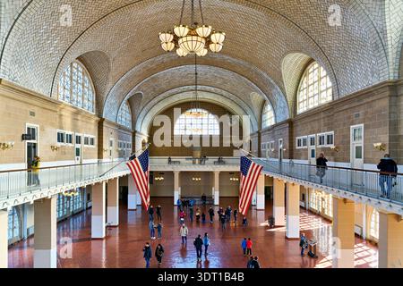Die Menschen laufen durch Ellis Island, eine historische Einwanderungsstation in Manhattan. Der Raum hat hohe Decken und große Fenster. Stockfoto