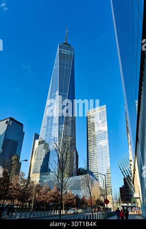 Die Menschen laufen in der Nähe des One World Trade Center mit klarem blauen Himmel darüber. Das National September 11 Memorial Museum ist in der Nähe und zieht Touristen an. Stockfoto