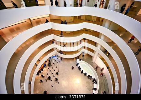 Die Menschen laufen durch das spiralförmige Design des Guggenheim Museums in New York. Der Raum umfasst Kunstausstellungen und Besucher, die die Aussicht genießen. Stockfoto