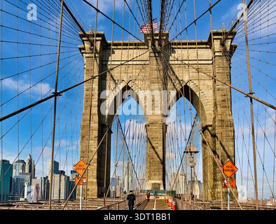 Die Menschen laufen über die Brooklyn Bridge in Manhattan und genießen an einem sonnigen Tag die Aussicht auf die Stadt und die Landschaft. Stockfoto