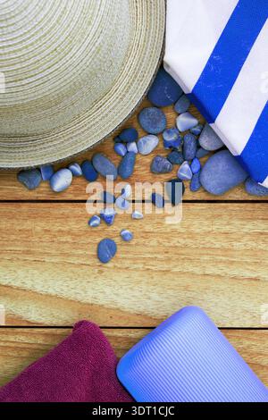 Sommerferienwohnung lag mit Strohhut, blauen Kieseln und Handtüchern auf Holz. Ideal für Reise-, Strand- und Lifestyle-Konzepte mit Kopierraum Stockfoto