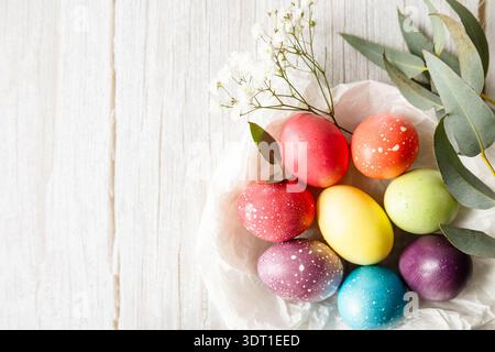 Pastellfarbene Ostereier mit Eukalyptusblättern und zarten weißen Blüten auf hölzernem Hintergrund. Sanftes Tageslicht, romantische Frühlingsatmosphäre mit Copy sp Stockfoto
