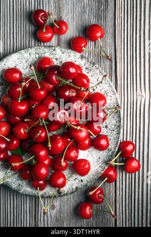 Blick von oben auf reife Kirschen, die auf hölzernem Hintergrund verstreut sind. Leuchtend rote süße Früchte, saisonales Erntekonzept Stockfoto