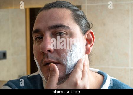 Erwachsener Mann, der Rasierschaum auf sein Gesicht in einem Badezimmer aufträgt Stockfoto
