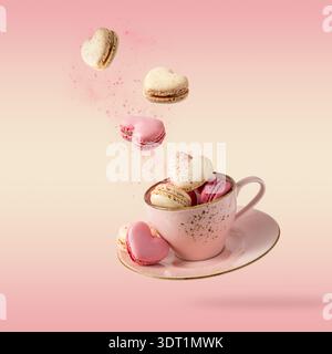 Französische süße bunte Kekse Macarons Makronen in Vintage rosa Tasse fliegen isoliert auf verlaufendem gelb rosa Hintergrund. Herzförmige Makronen Fallin Stockfoto