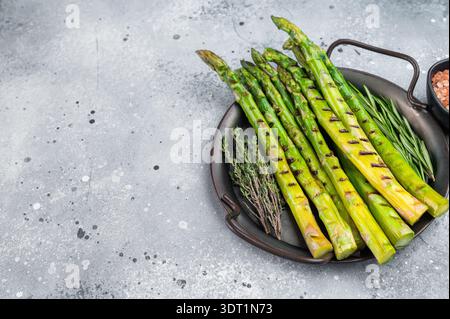 Geröstete Spargelstangen mit Grillspuren und Kräutern auf minimalem grauen Hintergrund, vegetarische Gourmet-Beilage im modernen Food-Stil. Stockfoto