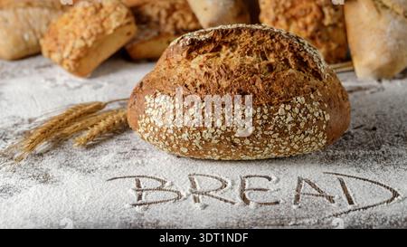 Ein Laib frisch gebackenes Mehrkornbrot auf dem Streumehl. Heller Hintergrund mit WORTBROT Stockfoto