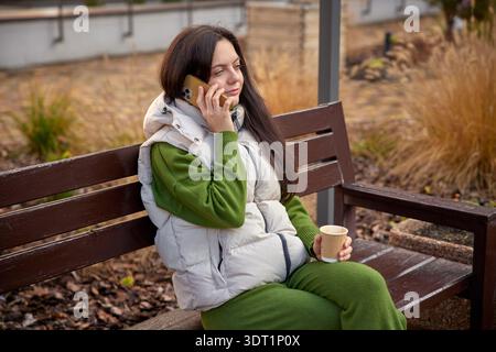 Frau, die sich im Freien mit Kaffee auf einer Bank unterhalten hat Stockfoto