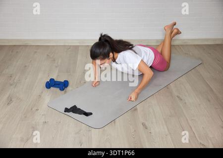 Frau, die auf Yogamatte mit Kurzhanteln in der Nähe trainiert, Liegestütze für Fitness Stockfoto