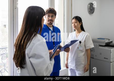Ein vielfältiges medizinisches Team aus zwei Ärzten und einer Krankenschwester führte ein Gespräch innerhalb eines Krankenhauses. Die Profis tragen Peelings und Labormäntel, Holdi Stockfoto