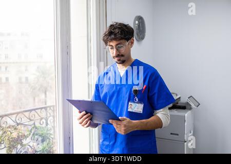 Ein medizinischer Fachmann in blauen Peelings prüft medizinische Dokumente in einem hellen Büro. Die Szene spiegelt ein modernes Gesundheitsumfeld wider und betont diese Stockfoto