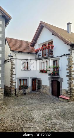 Malerisches Steinhaus in Ochagavia, Navarra, Spanien, geschmückt mit leuchtend roten Blumen auf Balkon und Fensterbänken. Eine typische rustikale Architektur auf einem Stockfoto