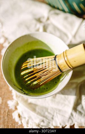 Eine Keramikschale gefüllt mit leuchtend grünem Matcha wird von einem traditionellen Bambusbesen begleitet. Dieses Setup zeigt den komplizierten Prozess der Herstellung von Matten Stockfoto