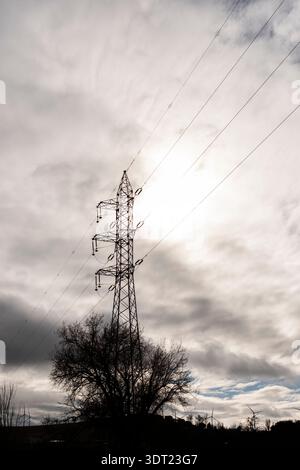 Silhouette einer gewaltigen Stromleitung vor dem Hintergrund eines dramatischen, bewölkten Himmels. Die Stahlkonstruktion steht hoch und schneidet die ausgedehnte graue Wolke Stockfoto