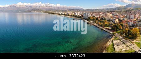 Aus der Vogelperspektive von Pogradec, Albanien, mit der Seepromenade, dem türkisfarbenen Wasser des Ohridsees und der Skyline der Stadt, die von Bergen umgeben ist. Stockfoto