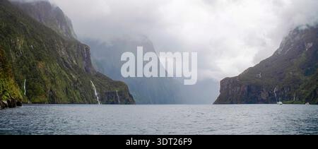 Der Milford Sound in Neuseeland besticht durch dramatische Klippen, die sich steil aus dem Wasser erheben, und üppige grüne Vegetation, die die Berghänge bedeckt. Stockfoto