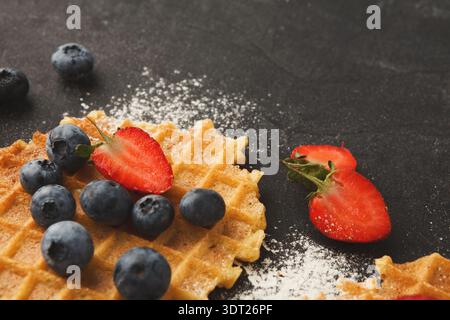 Erstellen Sie eine farbenfrohe Collage aus Waffeln mit frischen Beeren auf dunkler Oberfläche für Dessert-Ideen Stockfoto