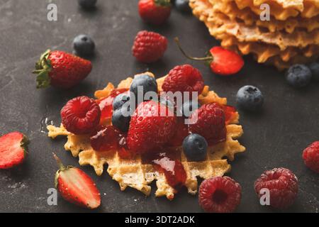 Köstliche Collage aus Waffeln mit frischen Beeren und Sirup auf dunkler Oberfläche Stockfoto