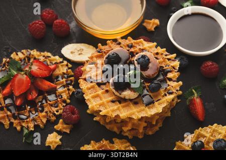 Sammlung von Waffeln mit Obst und Sirupe auf dunkler Oberfläche Stockfoto