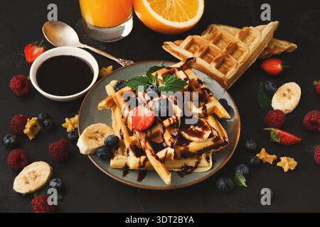 Köstliche Waffelcollage mit Obst und Sirup auf einem dunklen Tisch Stockfoto